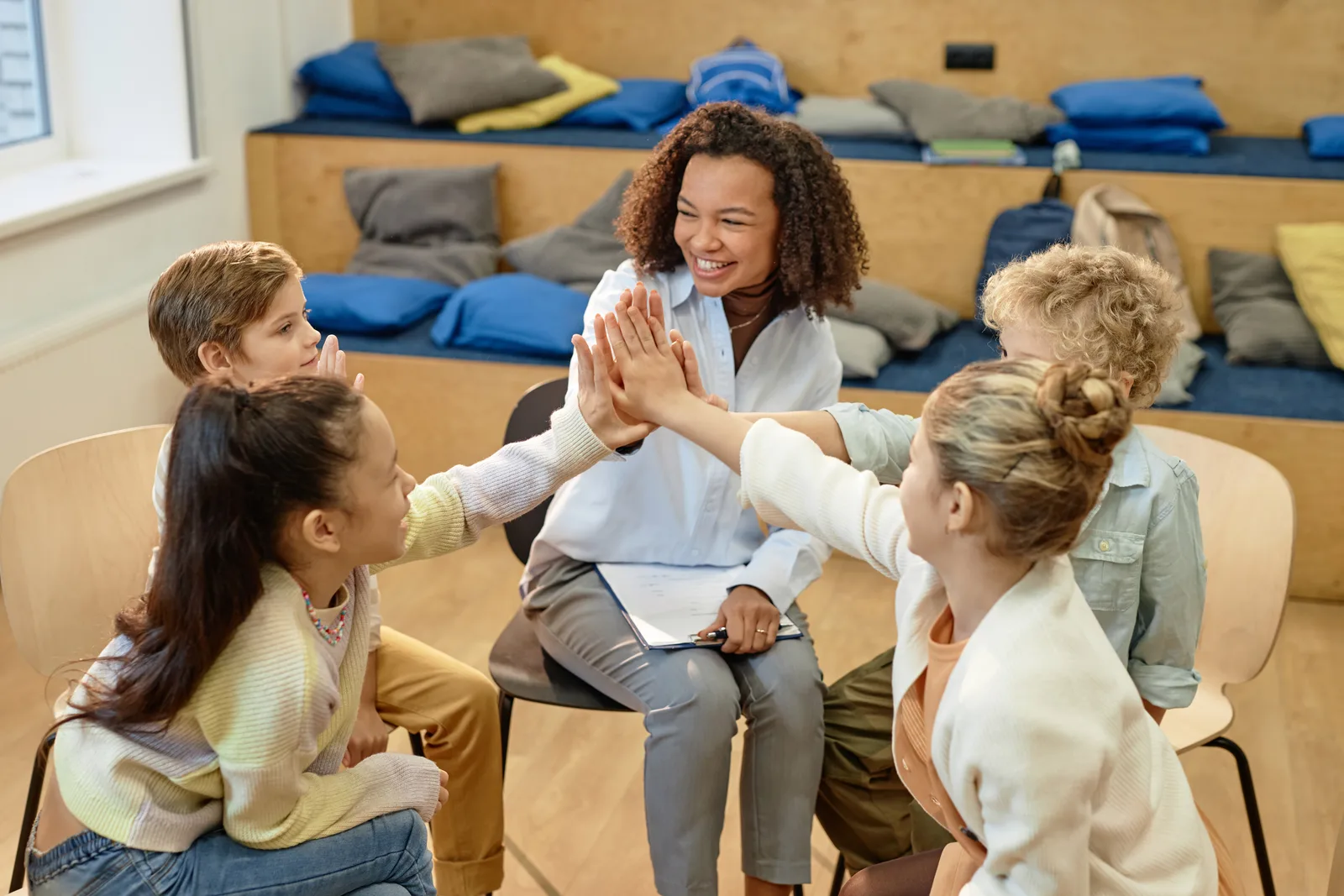 Une encadrante souriante tape dans les mains d’un groupe d’enfants réunis en cercle